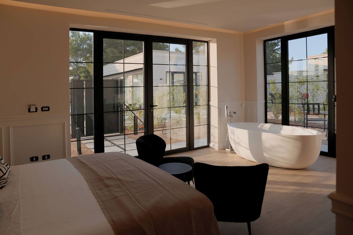 A modern hotel room with a large bed, a black chair, a round table, and a large bathtub.