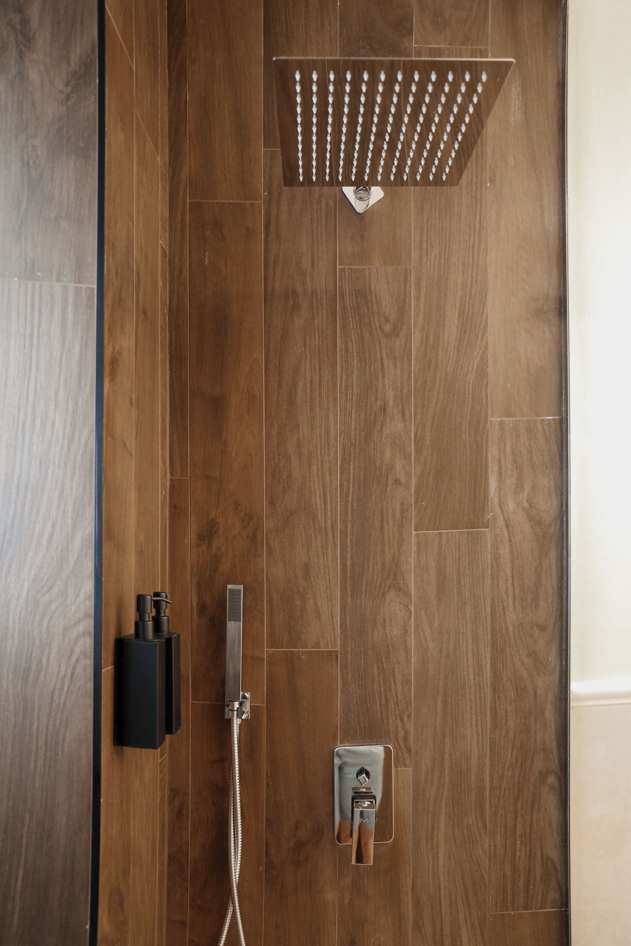 A shower with a rain showerhead and a handheld showerhead, both mounted on a wooden wall.