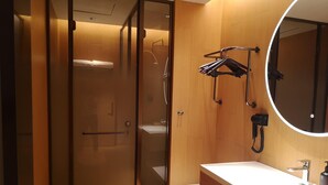 A modern bathroom with a glass shower enclosure, a wooden vanity, a round mirror, and a hairdryer mounted on the wall. - Ji Hotel Hangzhou Songcheng (Hangzhou)