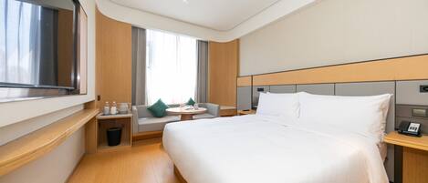 Una habitación de hotel moderna con una cama grande, una pequeña zona de estar, una mesita de noche y una ventana con cortinas.