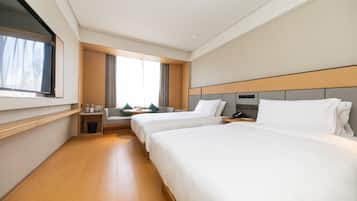 Habitación de hotel con dos camas, televisión, ventana con cortinas, una mesita con lámpara y mesita de noche con teléfono.