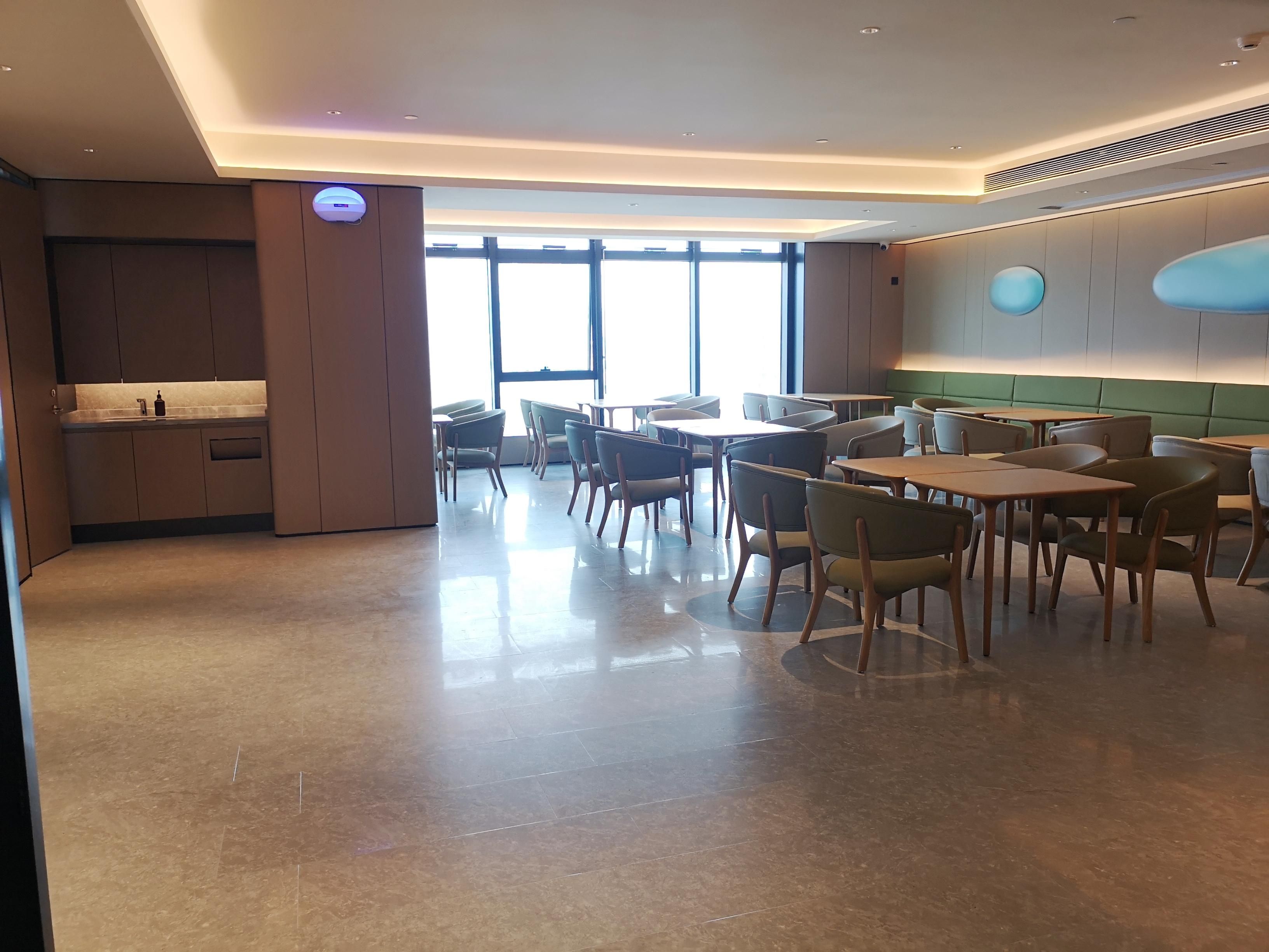 A modern dining area with tables and chairs, a kitchen area with cabinets, and large windows allowing natural light.