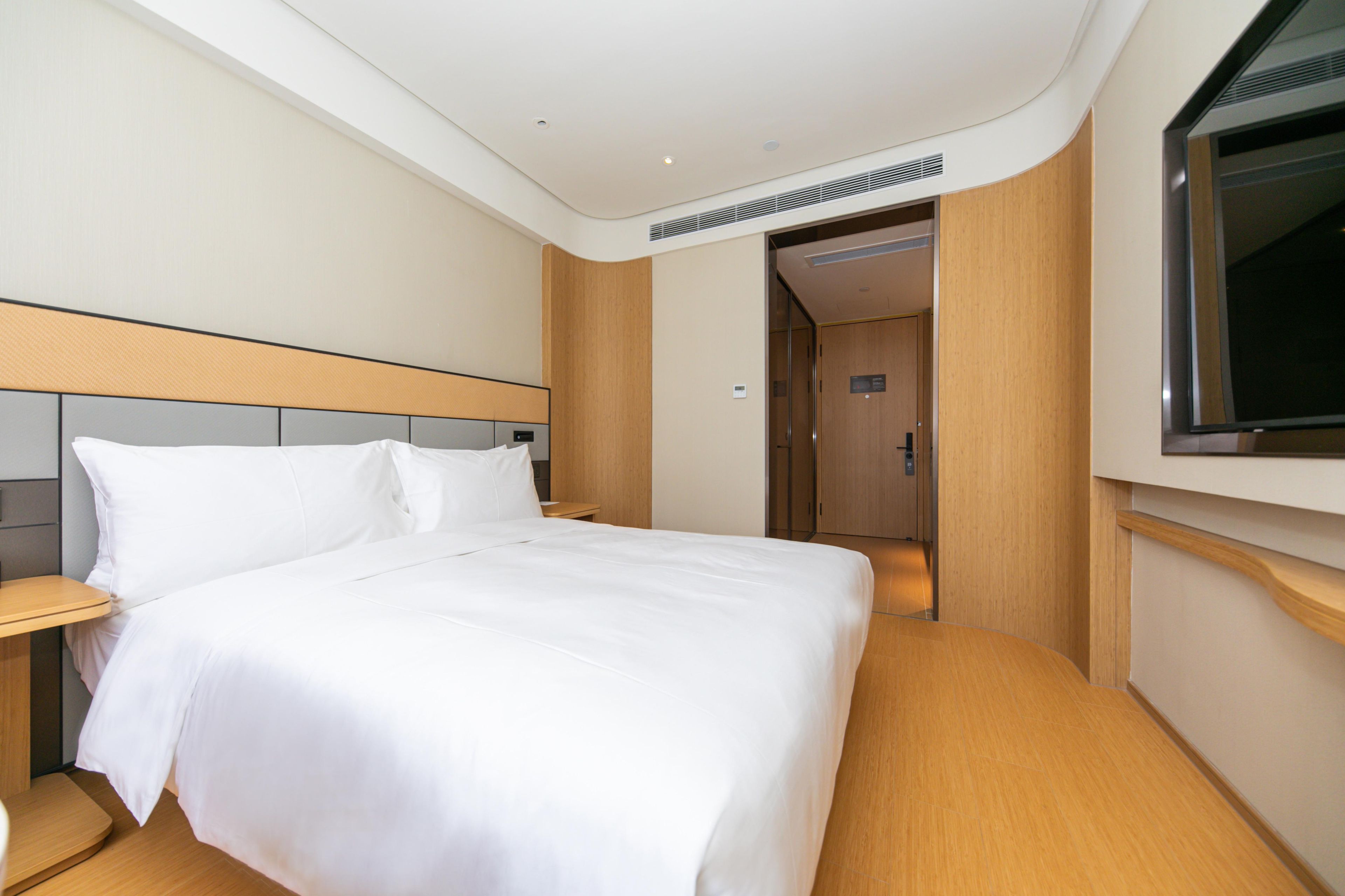 A hotel room with a large bed, a TV mounted on the wall, and a wooden headboard.