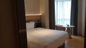 A hotel room with a large bed, a bedside table, a chair, a small round table, and a window with curtains.