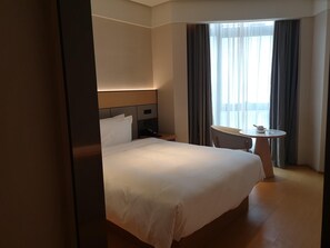 Ett hotellrum med en stor säng, ett sängbord, ett litet runt bord med en stol och ett fönster med gardiner.