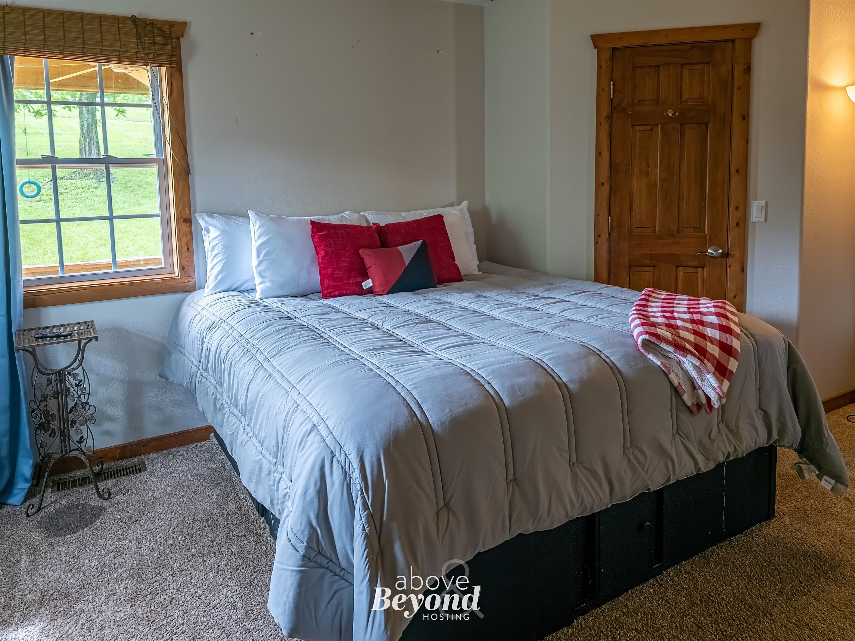 Un dormitorio con cama, ventana, puerta y una pequeña mesa.