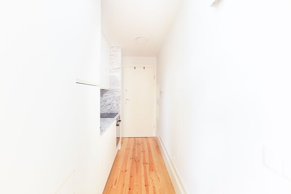 Un pasillo estrecho con suelo de madera y paredes blancas que conduce a una puerta.