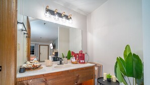 A bathroom with a large mirror, wooden vanity, and a modern light fixture above the mirror. - Peaceful Refuge minutes to SDC with Shuttle (Branson)