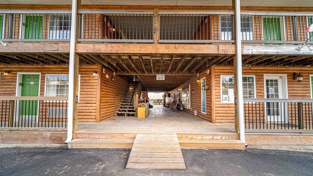 A two-story log cabin with a central staircase, wooden deck, and a sign indicating "Above Beyond Hosting". - Peaceful Refuge minutes to SDC with Shuttle (Branson)