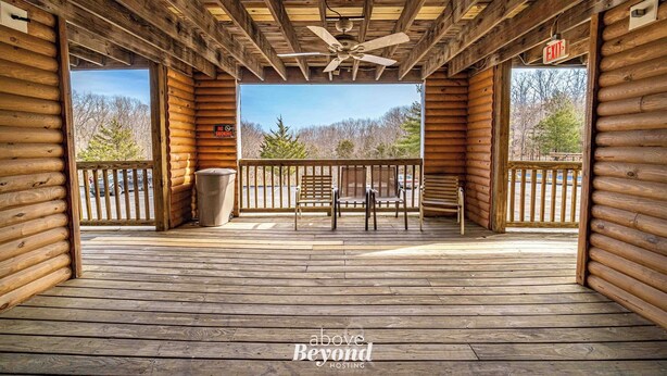 Una terraza de madera con ventilador de techo, banca y vistas a árboles y montañas.