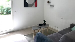 A modern living room with a grey sofa, a small round table with two stools, a potted plant, and a wall-mounted air conditioner. - Beach Cannes Bungalows (Le Cannet)