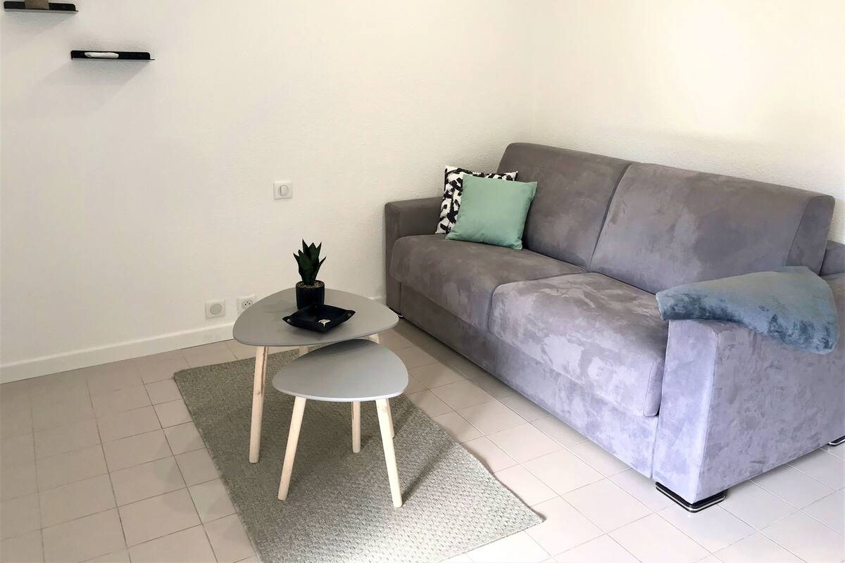 Una sala de estar moderna con un sofá gris, una pequeña mesa redonda y una alfombra gris.