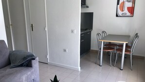 A modern living room with a grey sofa, a small round table with a plant, and a dining area with a table and chairs. - Beach Cannes Bungalows (Le Cannet)