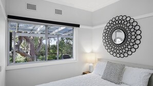 A bedroom with a large window, a round mirror, and a bed with pillows. - Secluded Family Retreat, Moments To Macs Beach (Macmasters Beach)