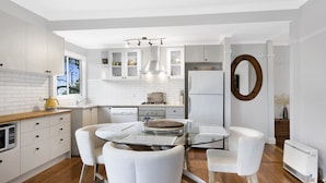 A modern kitchen with white cabinetry, a round glass table, and a built-in oven. - Secluded Family Retreat, Moments To Macs Beach (Macmasters Beach)