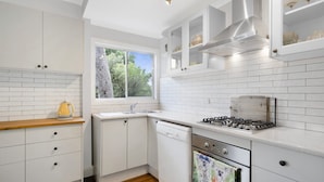 A modern kitchen with white cabinetry, a window, a gas stove, and a dishwasher. - Secluded Family Retreat, Moments To Macs Beach (Macmasters Beach)