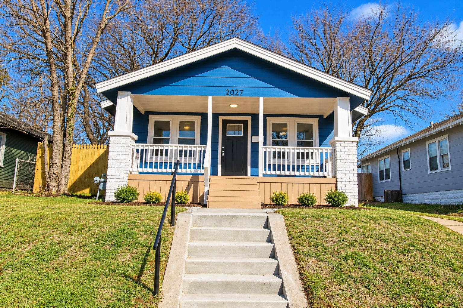 A two-story house with a blue exterior, white trim, and a front porch with a white railing.