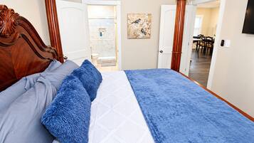Quarto com cabeceira de madeira, cama com roupa de cama azul e cinza e um quadro na parede.