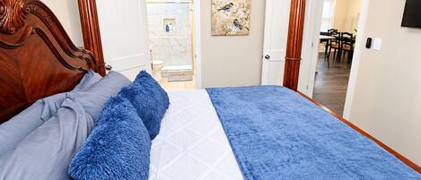 Een slaapkamer met een houten hoofdeinde, een bed met blauw-grijze beddengoed en een schilderij aan de muur.