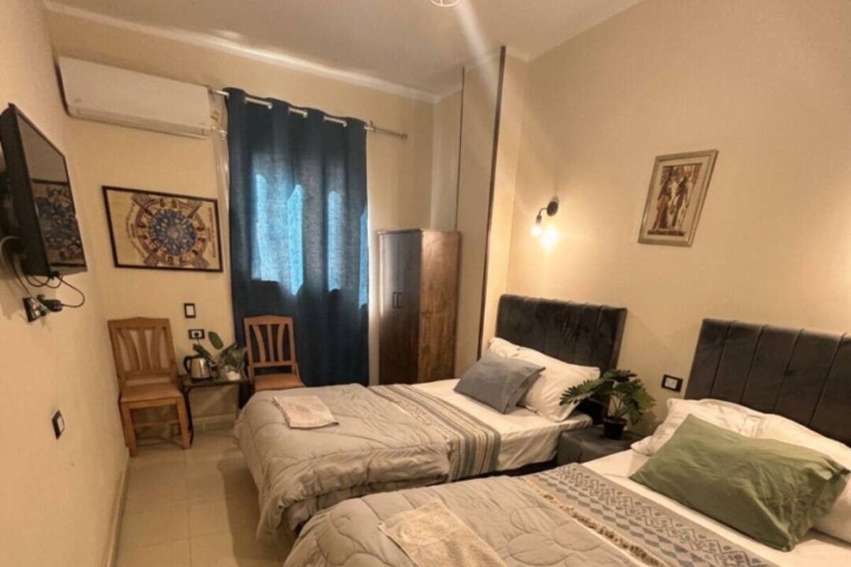 A bedroom with two beds, a small table, chairs, a wardrobe, and a mirror.