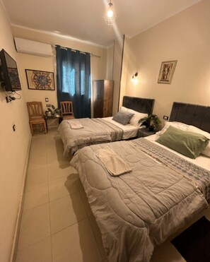 A bedroom with two beds, a small table, chairs, a wardrobe, and a mirror.