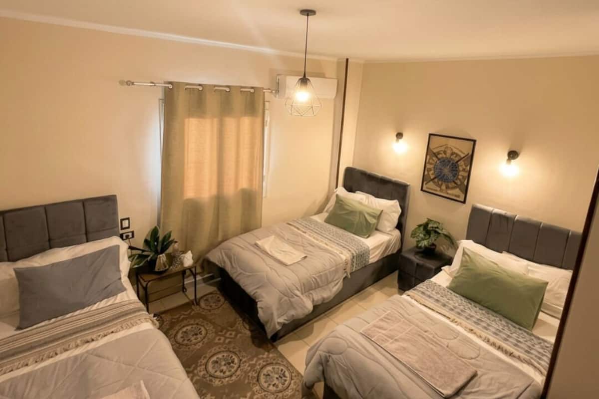 A bedroom with three beds, a patterned rug, a hanging light fixture, and a wall-mounted artwork.