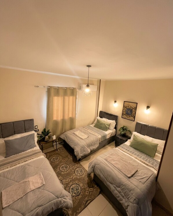 A bedroom with three beds, a patterned rug, a hanging light fixture, and a wall-mounted artwork.