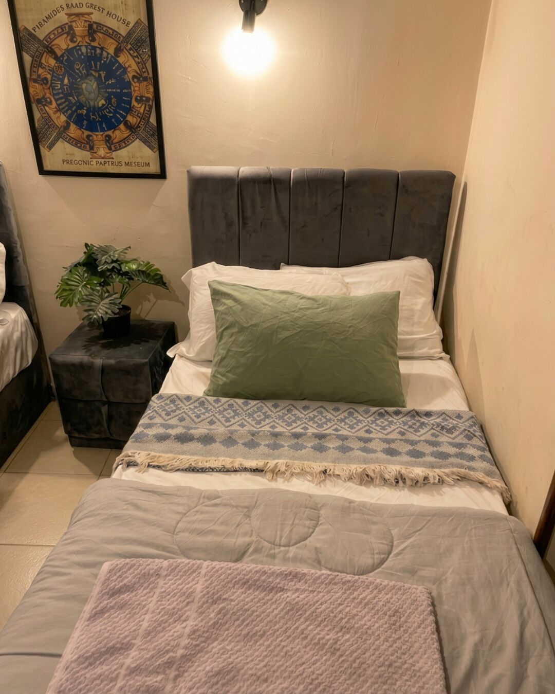 A bedroom with a bed, a nightstand with a plant, and a wall-mounted light fixture.