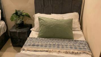 A bedroom with a bed, a nightstand with a plant, and a wall-mounted light fixture.