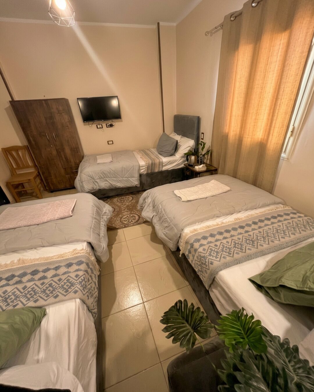 Ein Schlafzimmer mit zwei Betten, einem Fernseher, einem Kleiderschrank und einer Pflanze.