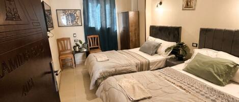 A bedroom with two beds, a wardrobe, a chair, a desk, and a door with a nameplate.