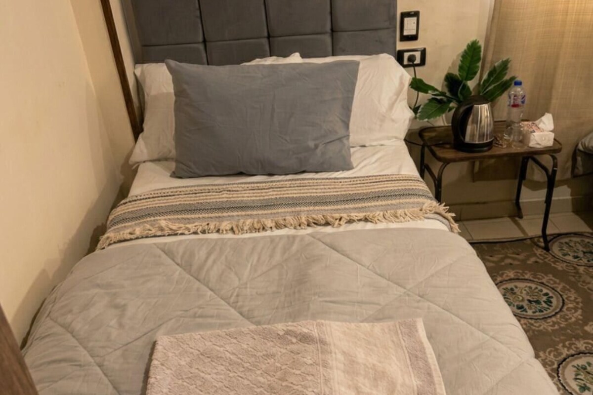 A bed with a grey headboard, a grey pillow, a beige blanket, and a folded towel.