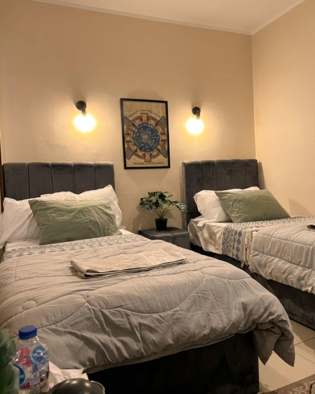 A hotel room with two beds, a wall-mounted artwork, and two wall sconces.