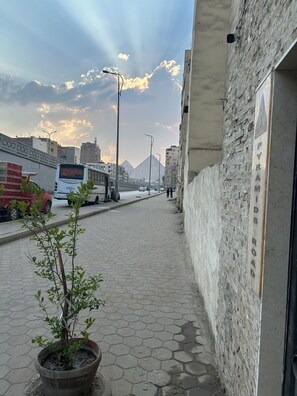 A paved street with a potted plant, a bus, and a building with a sign reading "PYRAMIDS ROAD".