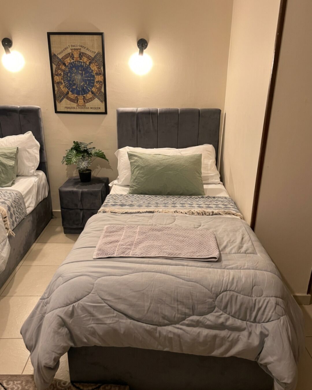 Une chambre à coucher avec un grand lit, deux tables de chevet, une plante en pot et un tableau encadré au mur.