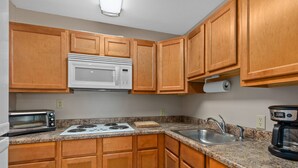 A kitchen with wooden cabinets, a microwave, a stove, a sink, and a coffee maker.