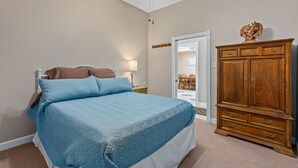 A bedroom with a bed, a wooden dresser, a ceiling fan, and a door leading to a bathroom.