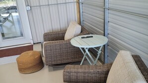 A wicker sofa set with cushions, a small round table, and a woven ottoman in a covered outdoor area with a sliding door.