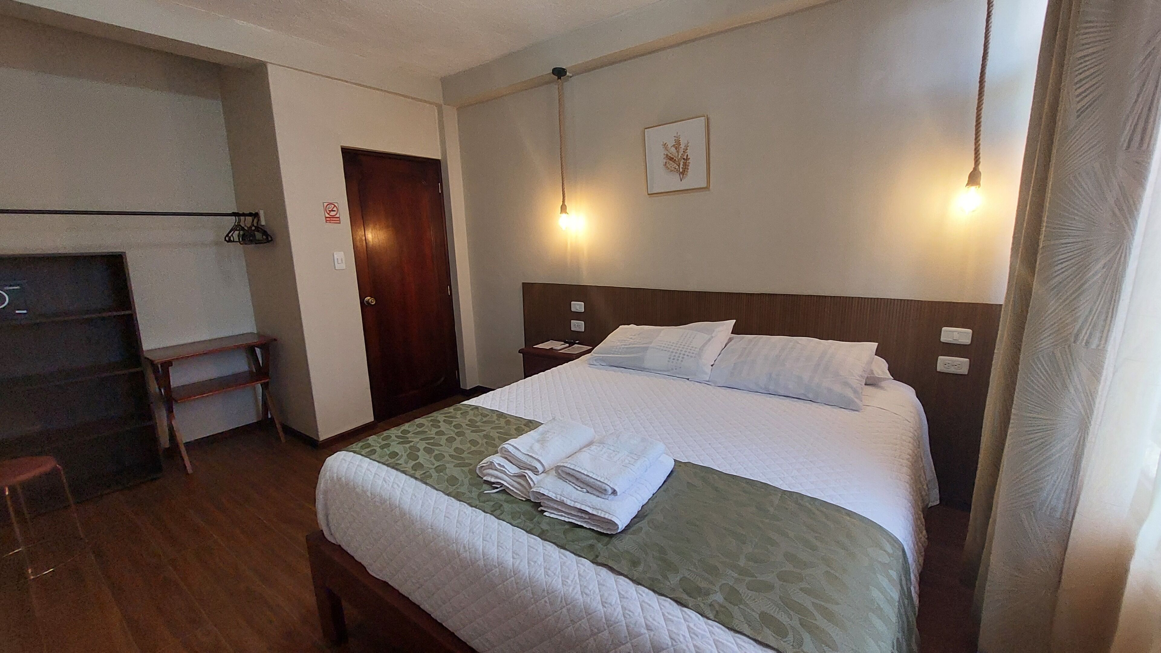 A hotel room with a bed, a nightstand, a desk, and a door.