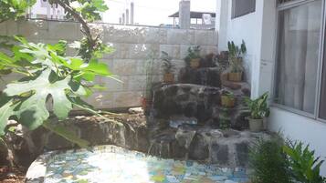 A small outdoor area with a tiled floor, a stone wall, and several potted plants.
