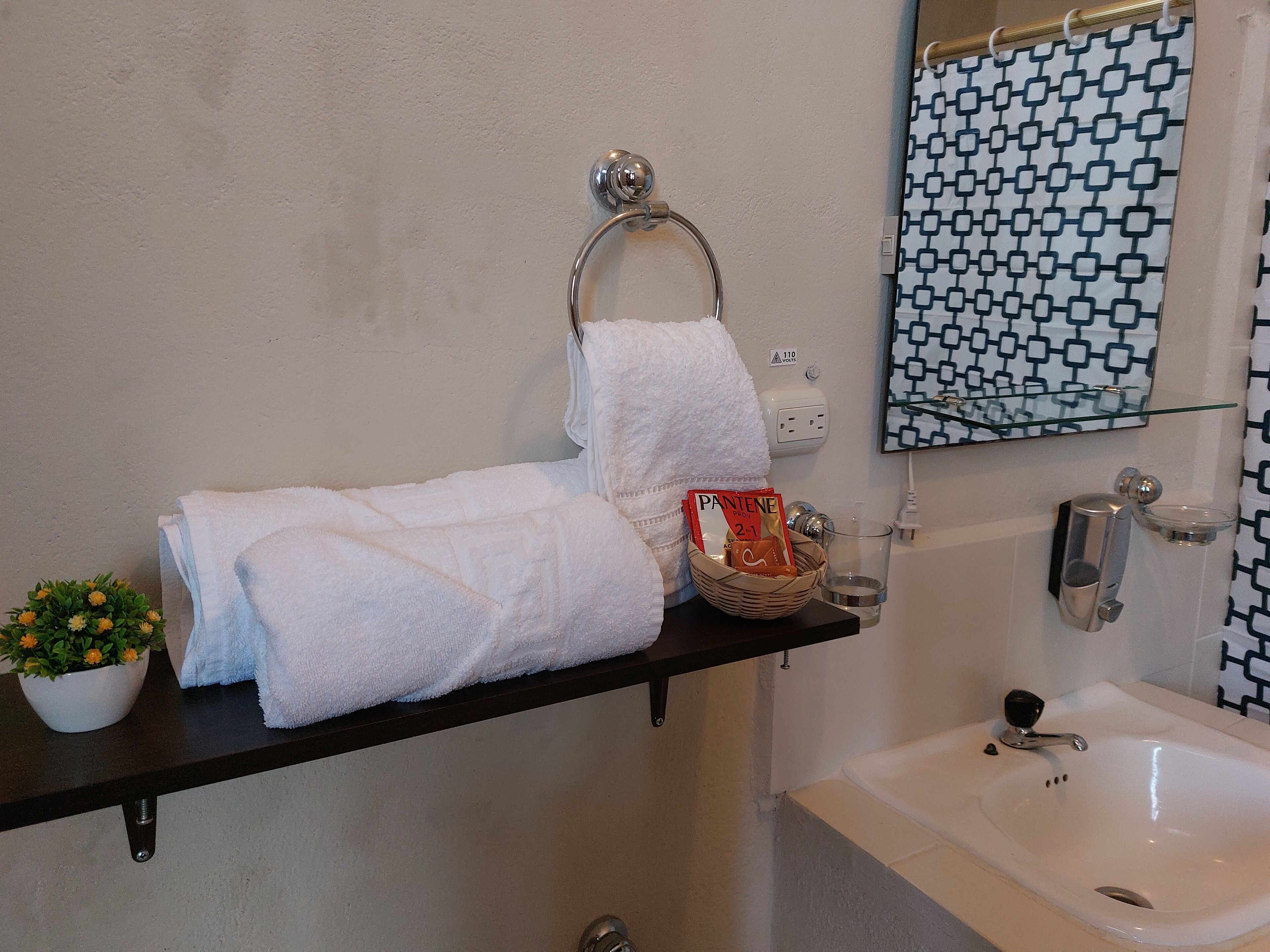 A bathroom with a white sink, a mirror with a geometric pattern, and a towel rack with folded towels.