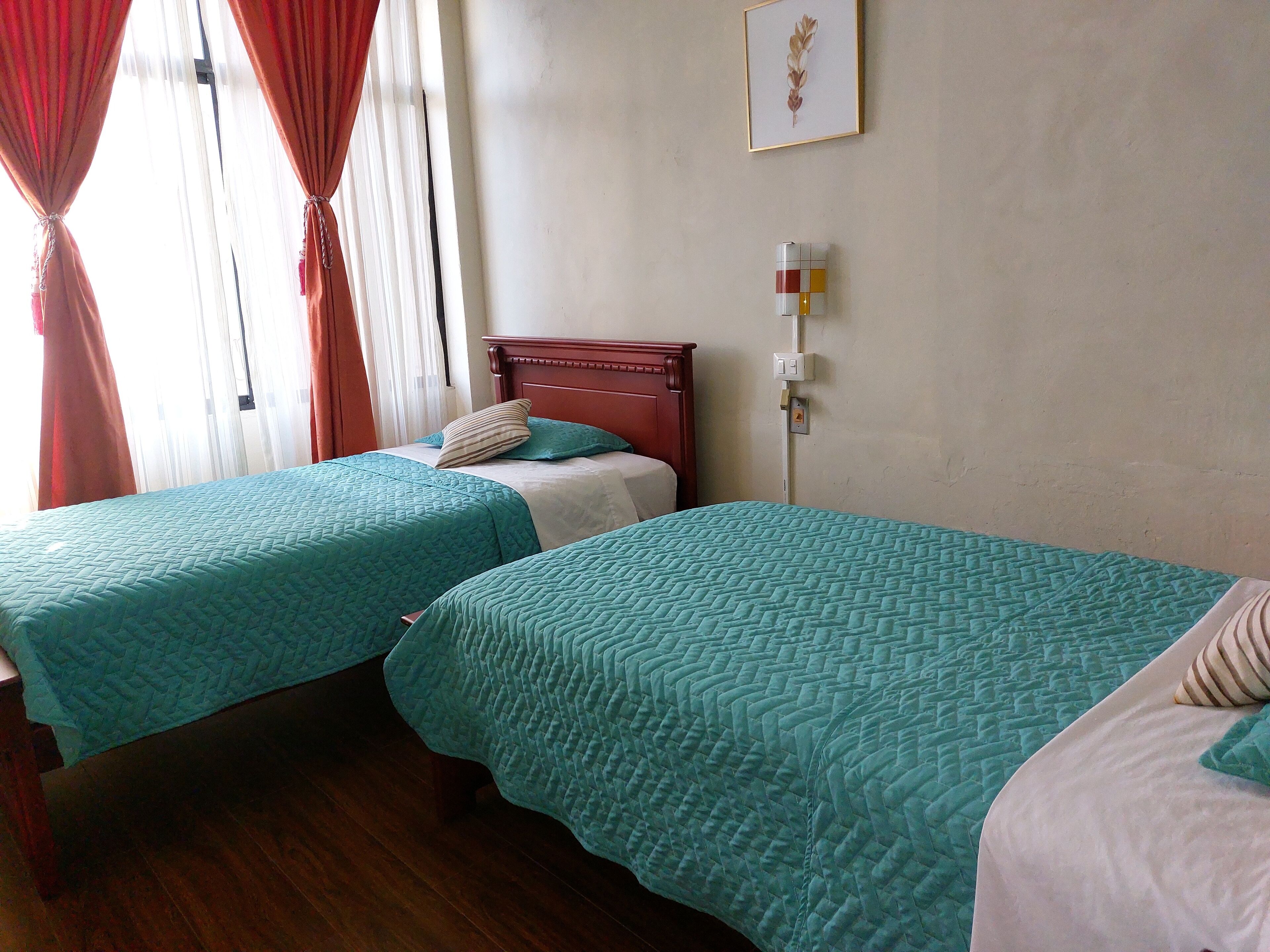 Una habitación de hotel con dos camas, cada una con ropa de cama color aguamarina, cabeceros de madera y una obra de arte enmarcada en la pared.