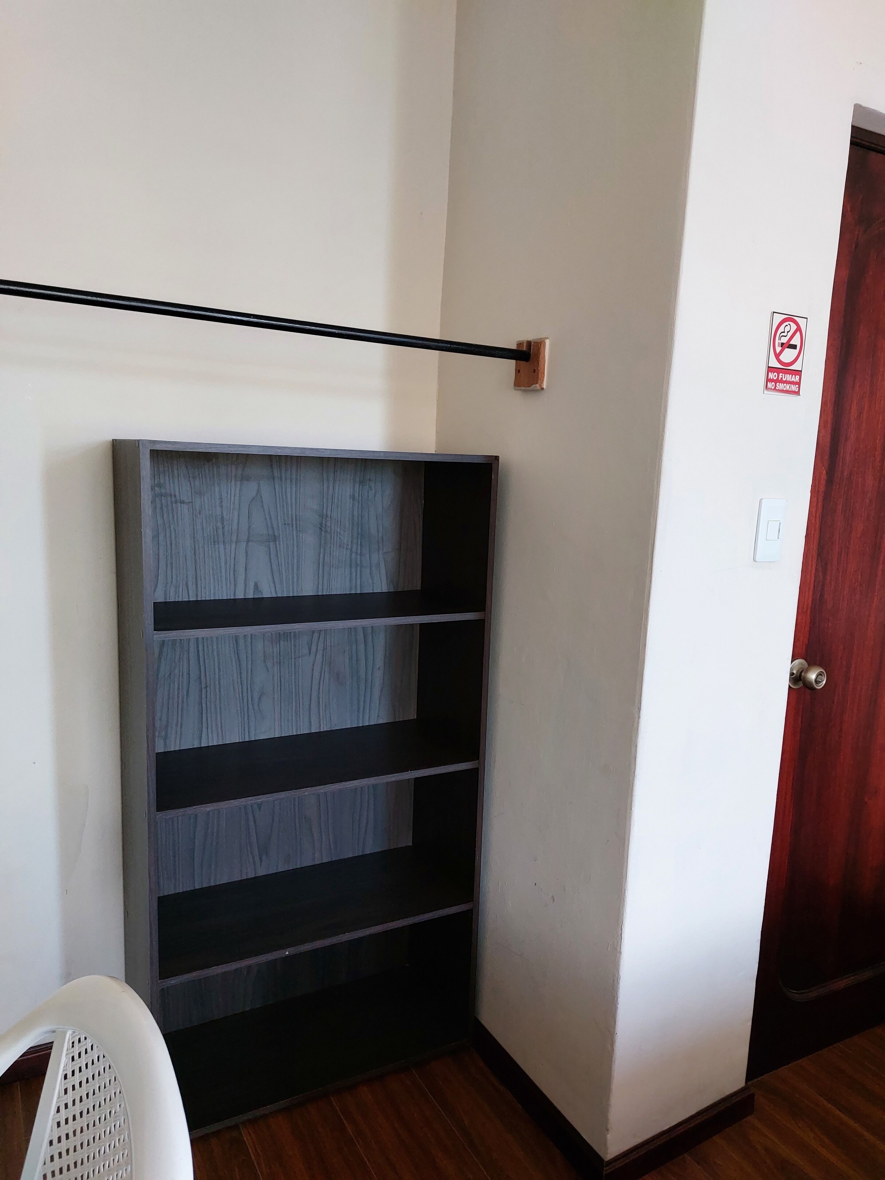 Ein Eckzimmer mit einer dunklen Holzeinrichtungsregal an der Wand, einem weißen Stuhl und einer Holztür mit einem Rauchverbot-Schild.
