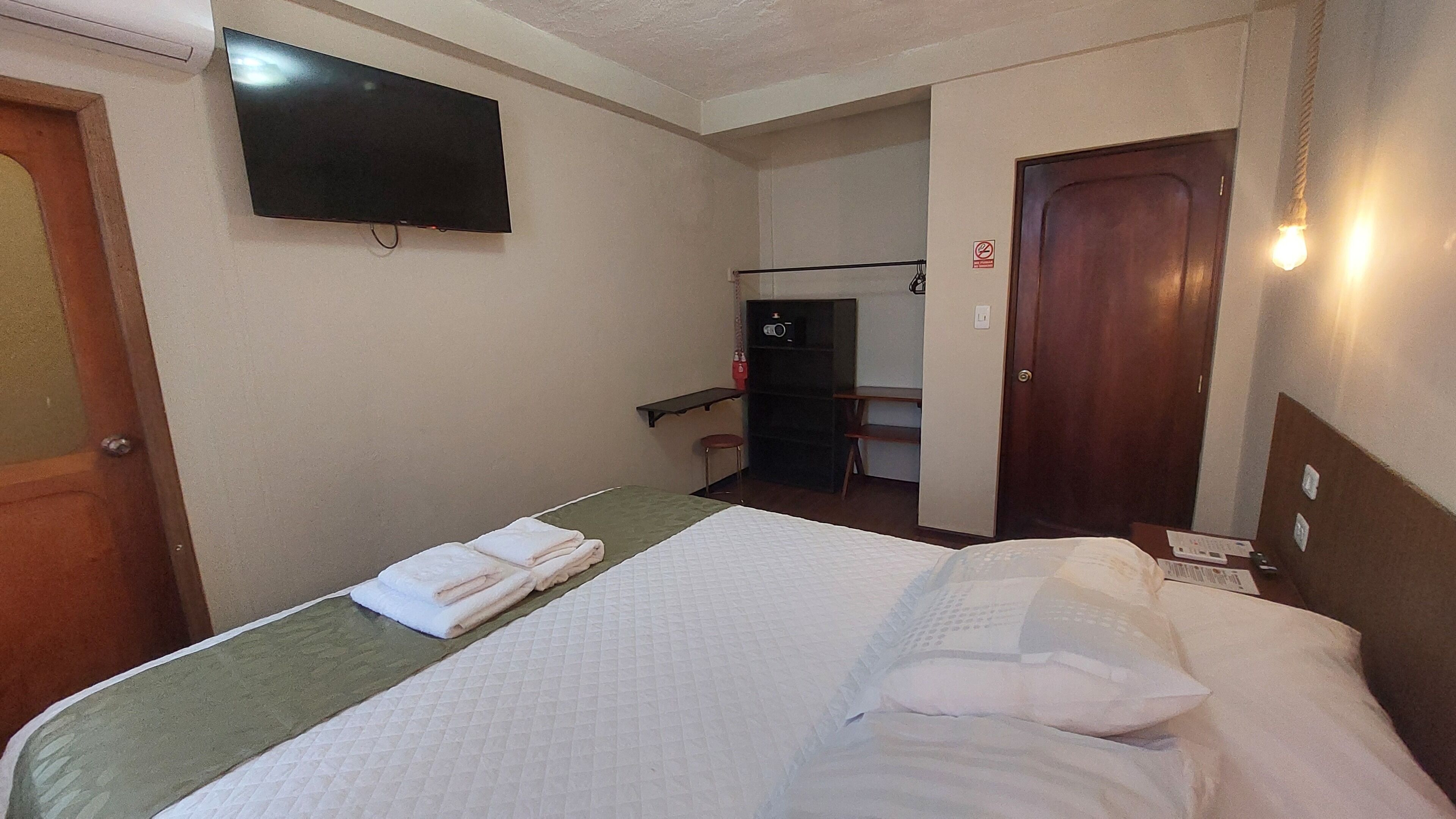 Une chambre d’hôtel avec un lit, un téléviseur fixé au mur, un bureau avec une chaise et une porte.
