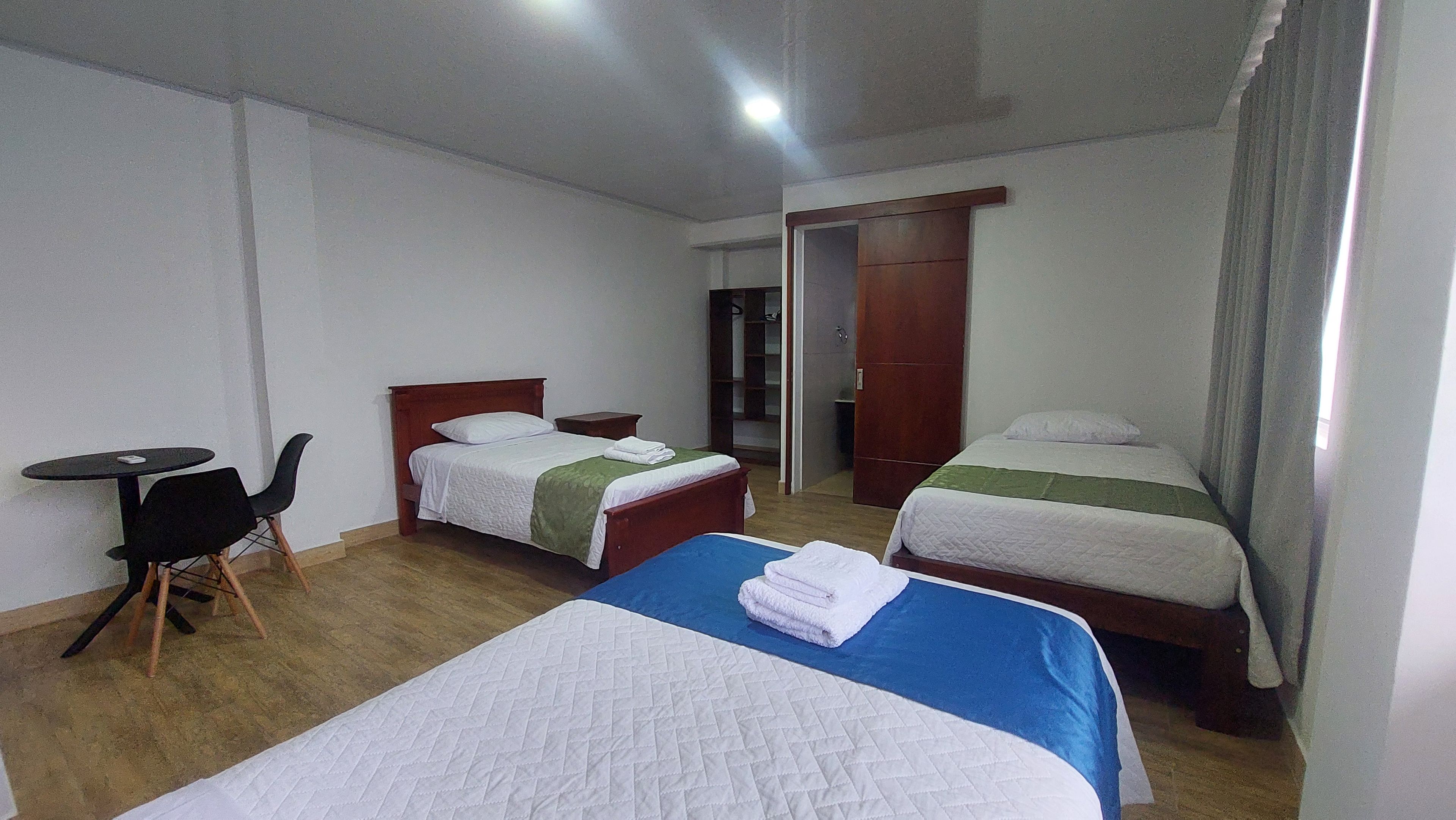 A hotel room with two beds, a small table, a chair, and a wardrobe.
