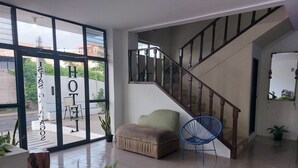 A hotel lobby with a staircase, a seating area with a cushioned bench and a chair, and a large window with a view of the street. - Hotel Islas Galapagos (Puerto Baquerizo Moreno)