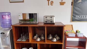 Una cuina americana amb nevera, microones i torradora. Hi ha prestatges amb tasses i plats, i un dispensador d'aigua. A la paret hi ha un cartell de 'Cafe & Te' i un mapa.