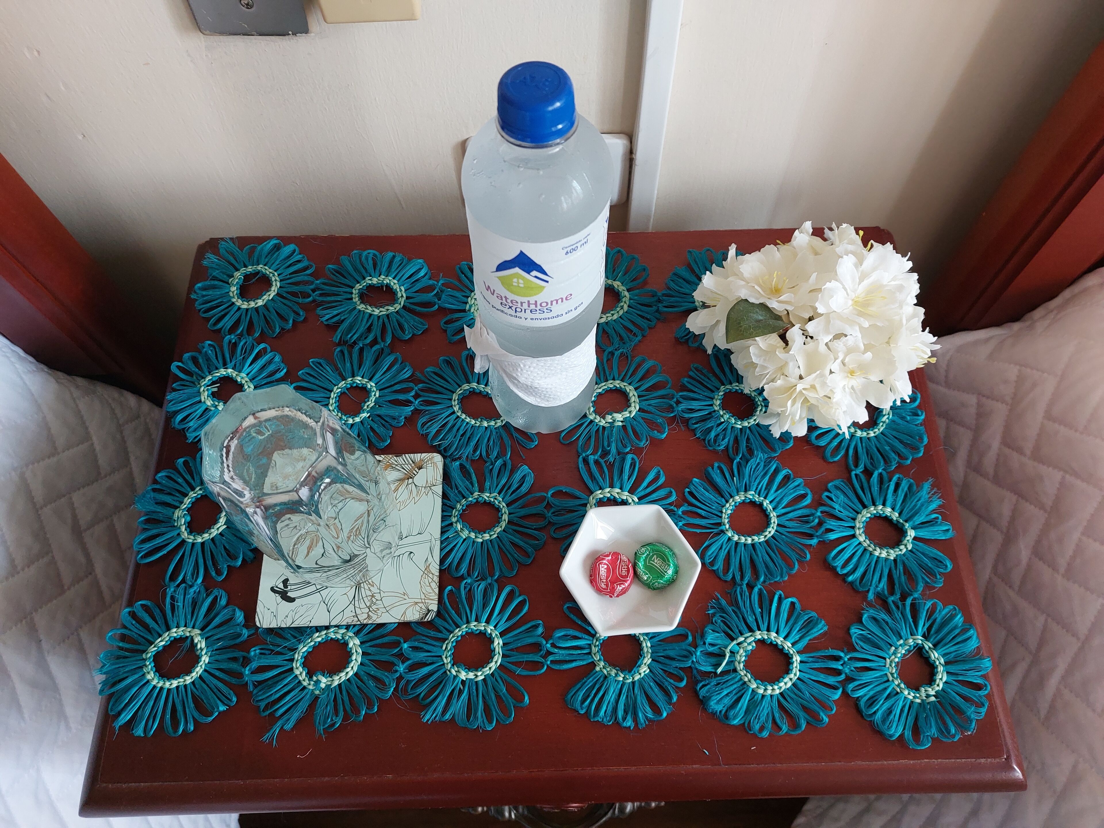 Una mesa con una botella de agua azul, una tarjeta y un plato pequeño con dos caramelos.
