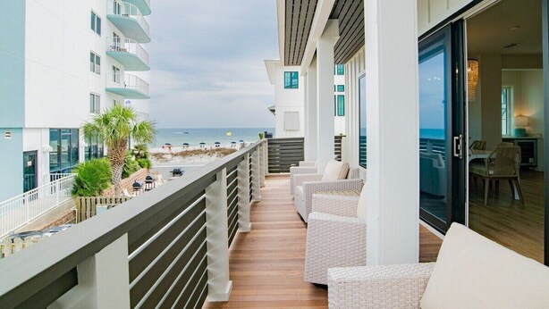 Un balcon agrémenté de meubles en osier, une vue sur la plage et un immeuble doté de balcons.