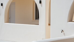 Um edifício branco com janelas em arco e uma porta, um pequeno objeto preto na parede, e um céu azul claro.